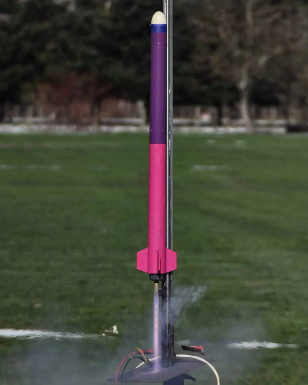 A purple and pink rocket lifting off the rail in a cloud of smoke