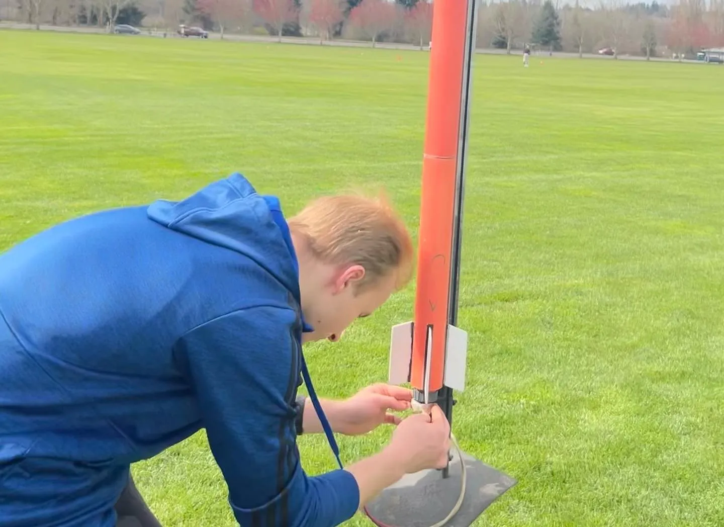 A student bending over a rocket on the pad in a grassy field